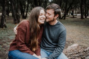 Romantic embrace between couple in casual attire against wooded background.