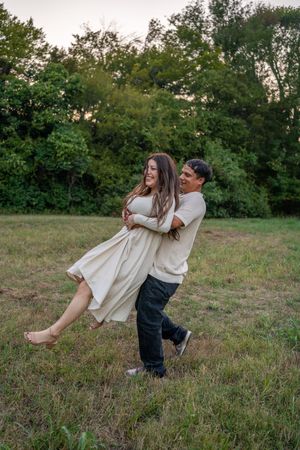 A couple performs a romantic dance lift in a grassy field at dusk.