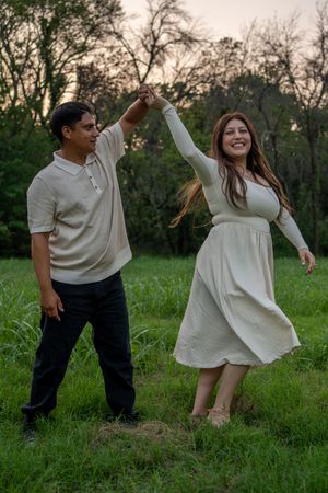 A couple shares a playful dance moment in a grassy field during sunset.