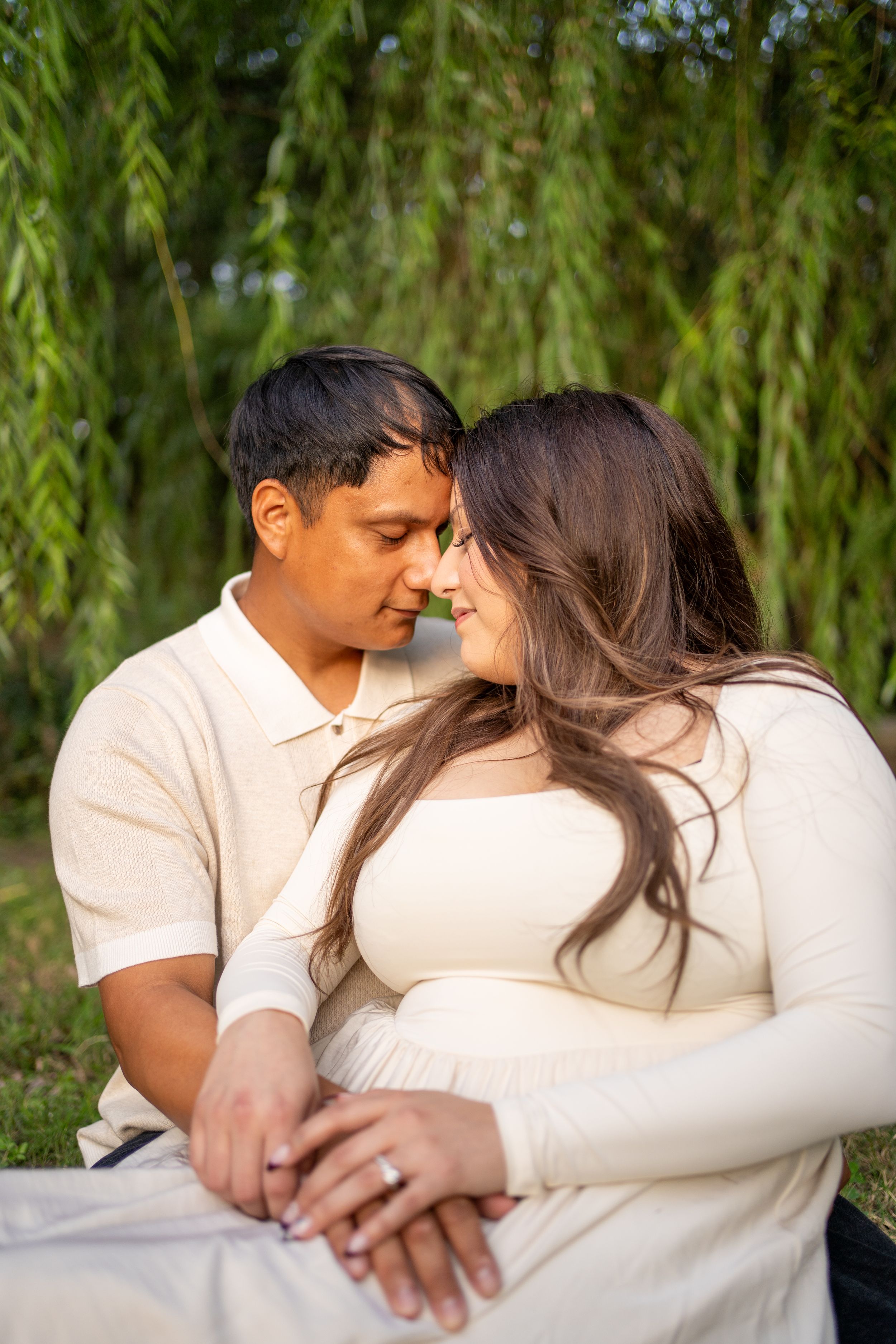 A tender moment between a couple sitting against a backdrop of willow trees.