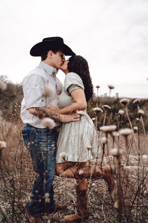 Romantic couple embracing in rustic field of dried flowers during golden hour.