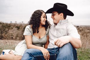 Western-themed couple portrait with cowboy hat against white background.