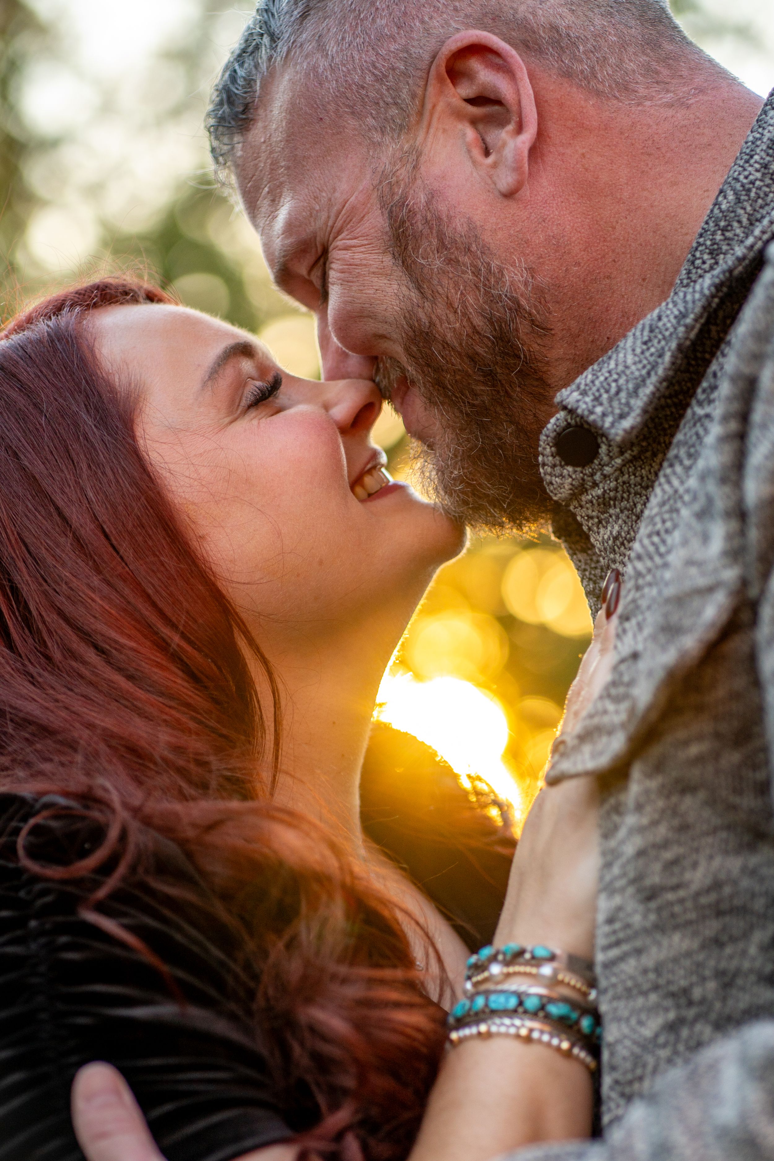 Intimate couple portrait with golden sunlight filtering through trees in background.