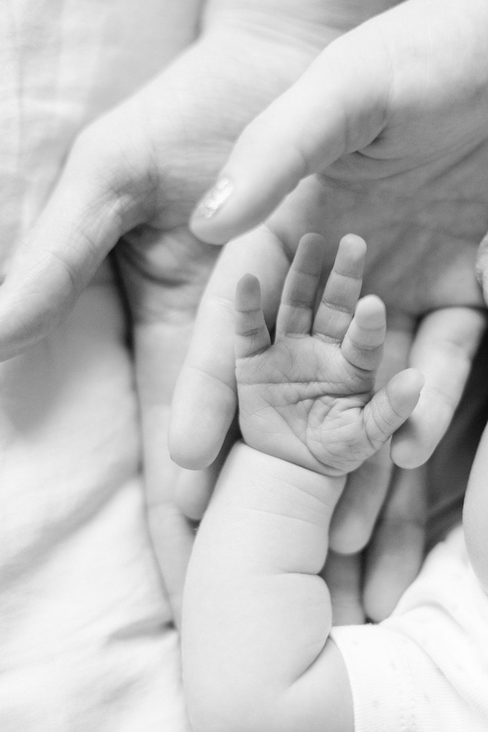 A sleeping newborn baby in white clothing being gently cradled by caring hands in a black and white photograph.