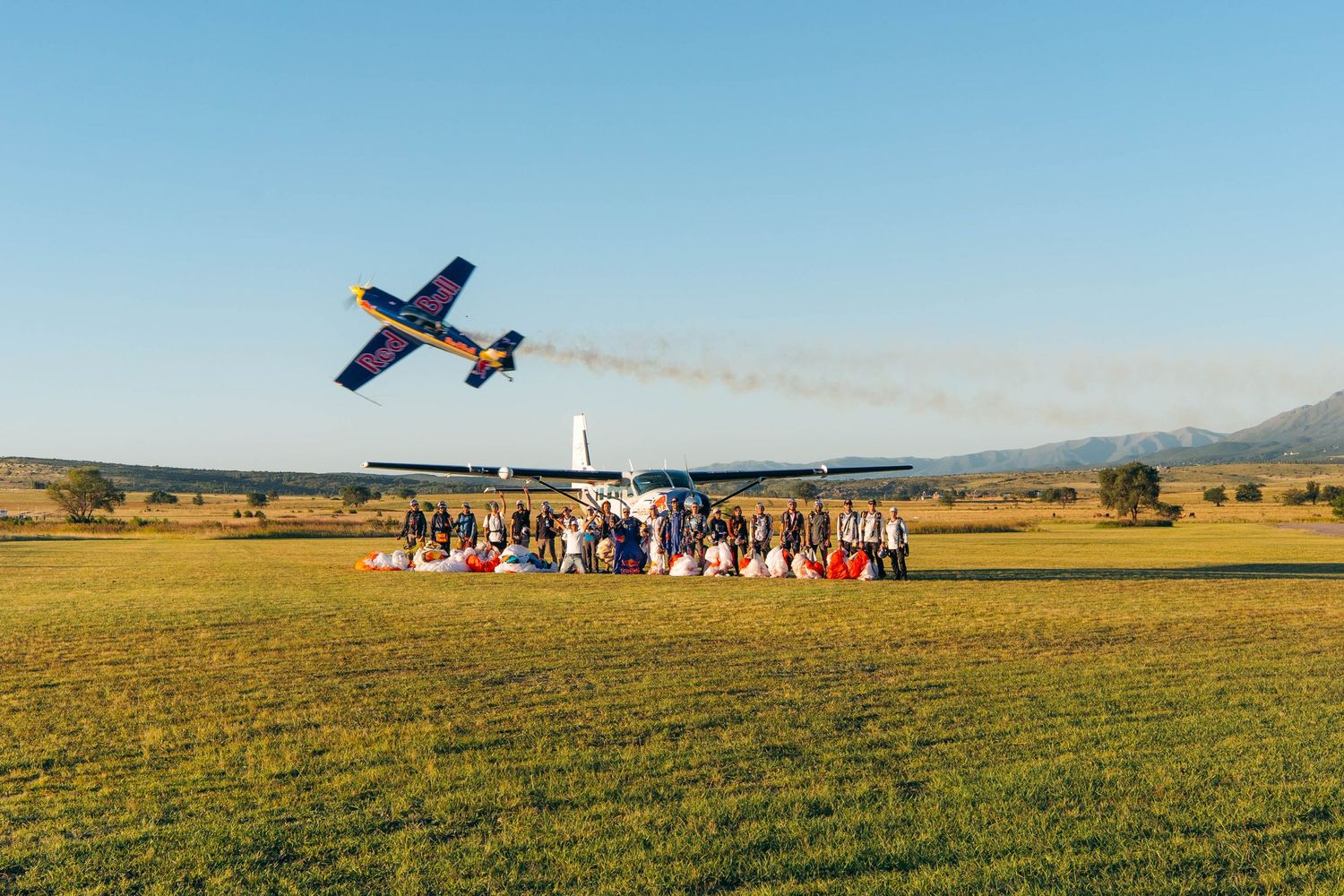 An aerobatic plane flies low over spectators at an airshow in a rural field.