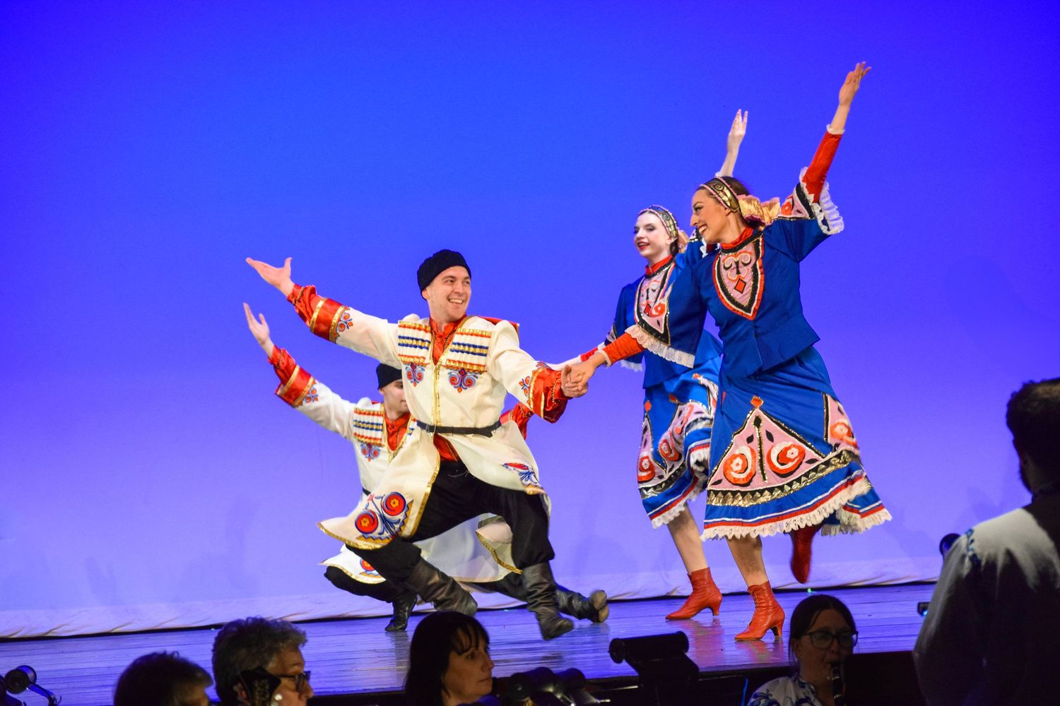 Dancers perform an energetic routine against a vibrant blue backdrop on stage.