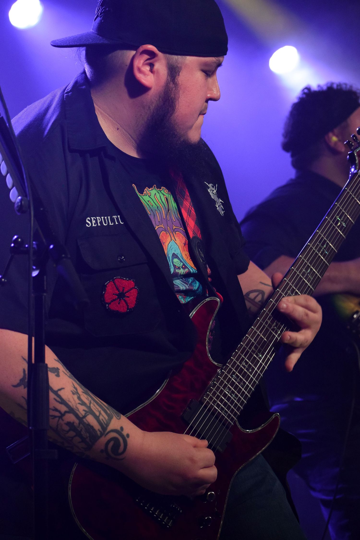 Musicians perform on stage with guitars under dramatic purple lighting.