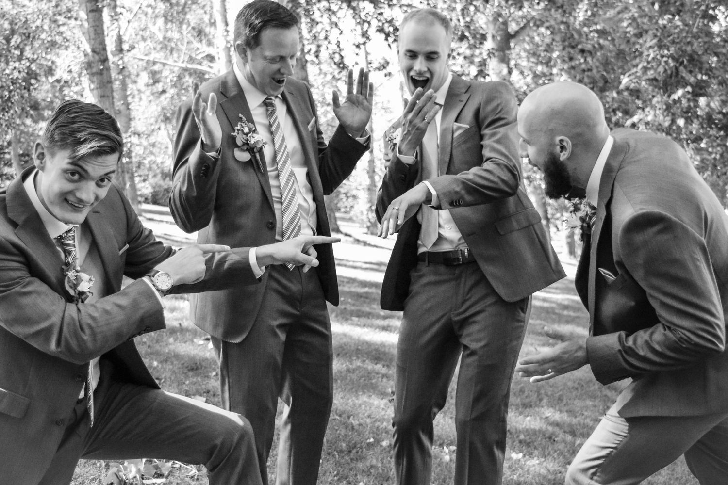 Groomsmen strike playful poses in formal attire during outdoor photo session.