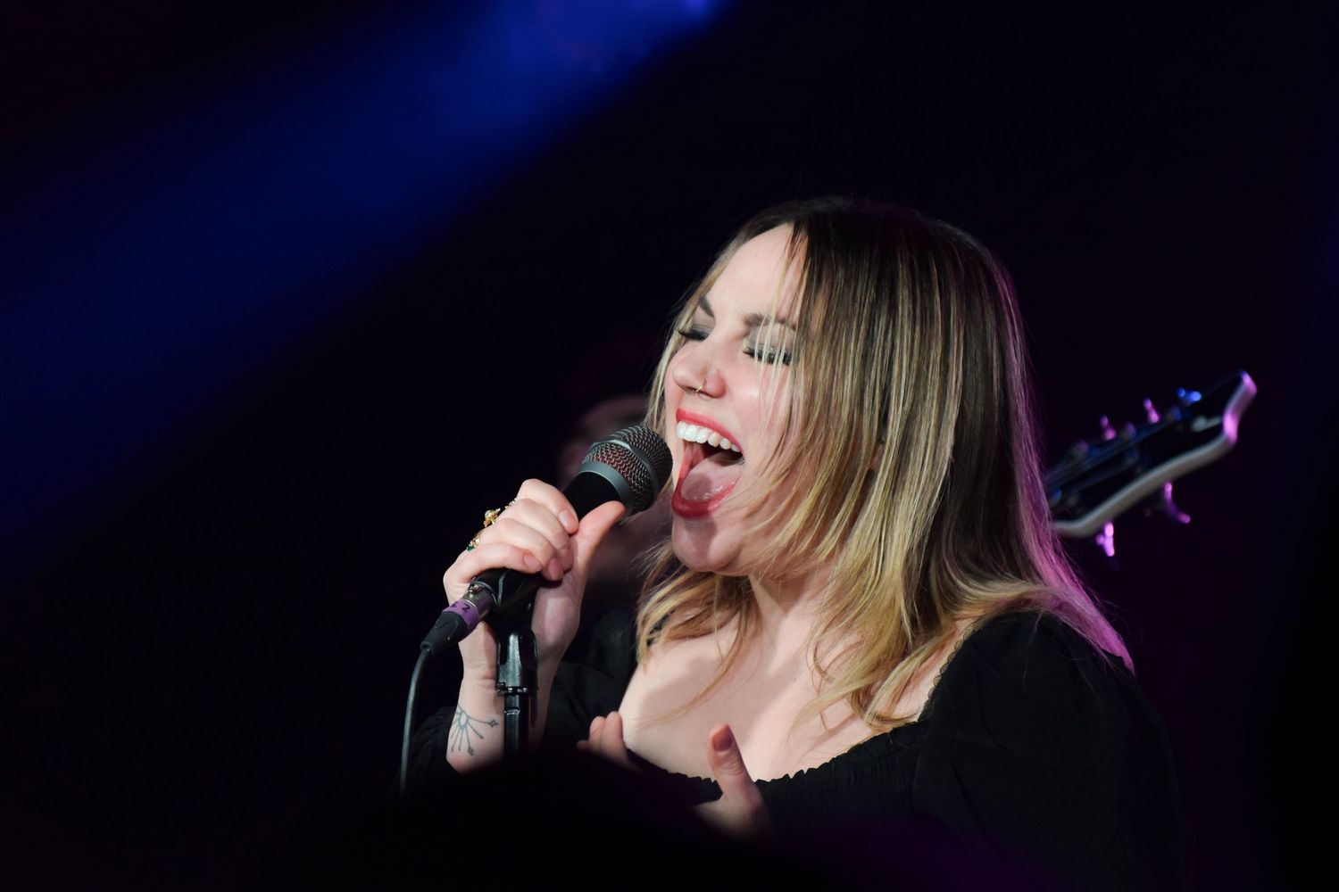 Concert performer singing on stage with dramatic blue backlighting.