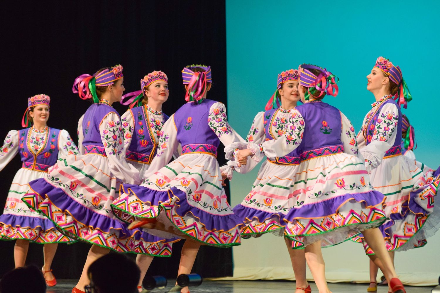 Ukrainian dancers in colorful traditional dresses perform a synchronized line dance routine.
