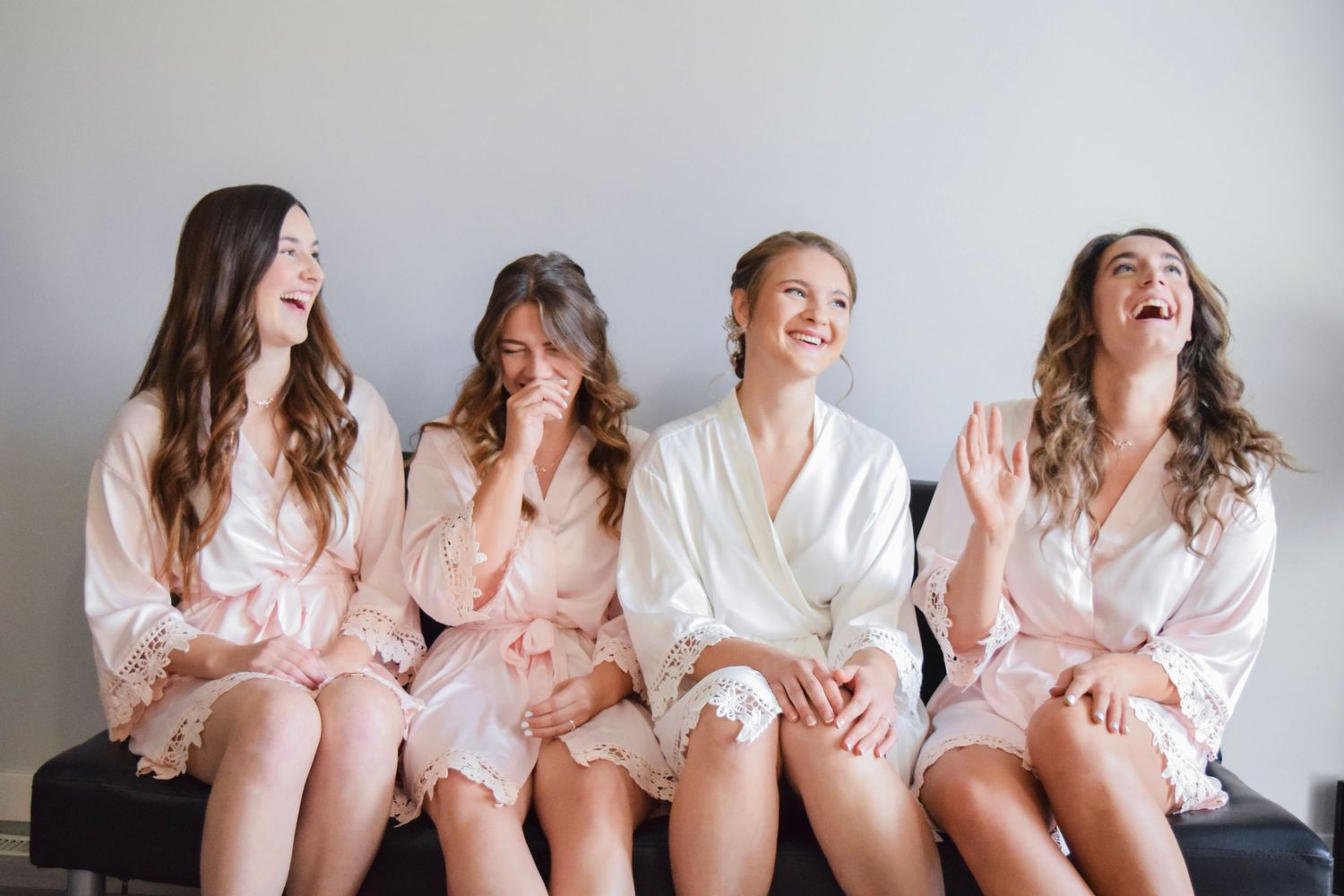 Bridesmaids wearing matching robes sits together sharing laughter during wedding preparations.
