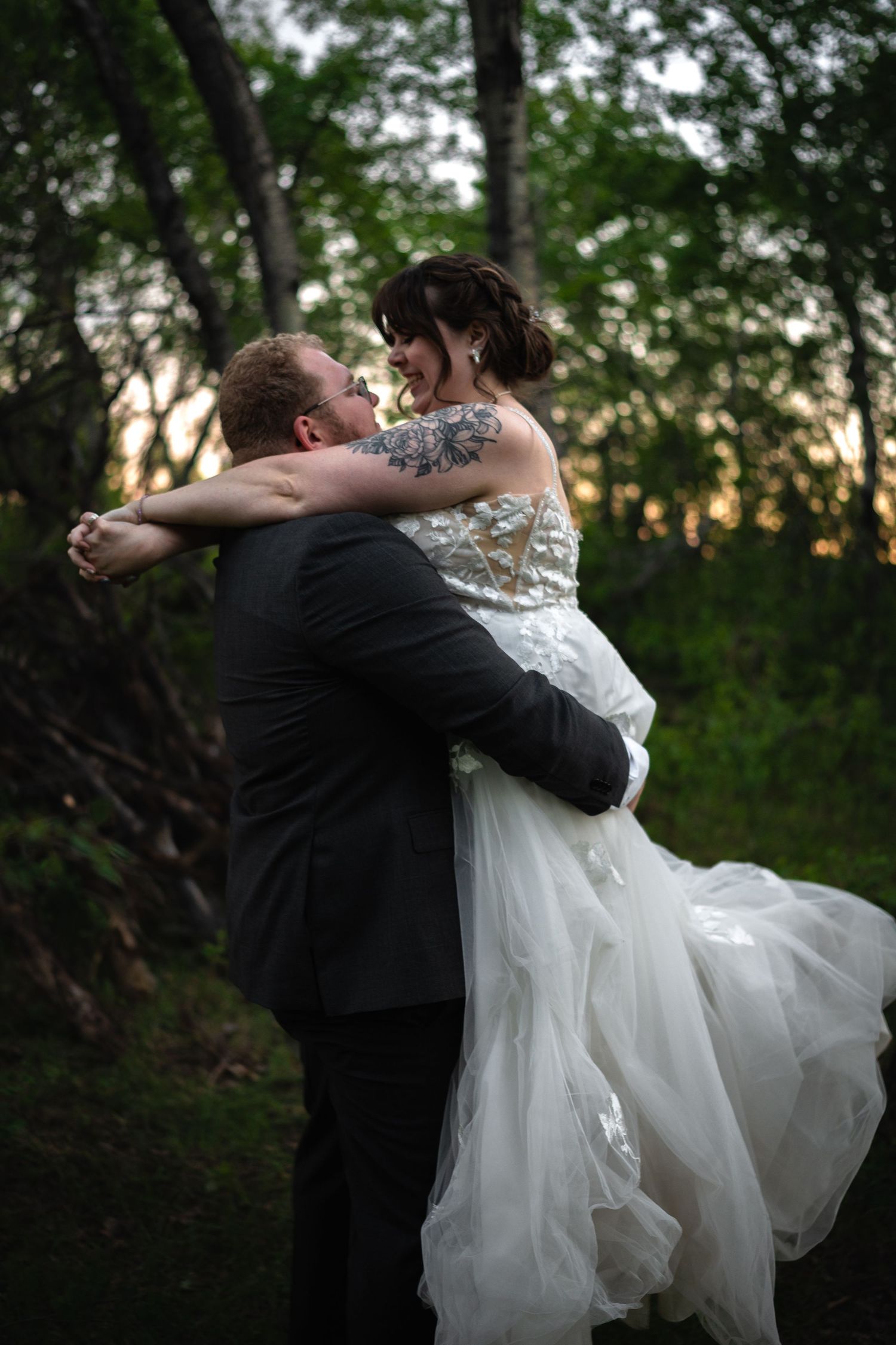 Romantic wedding couple embracing during sunset photoshoot in a wooded area.