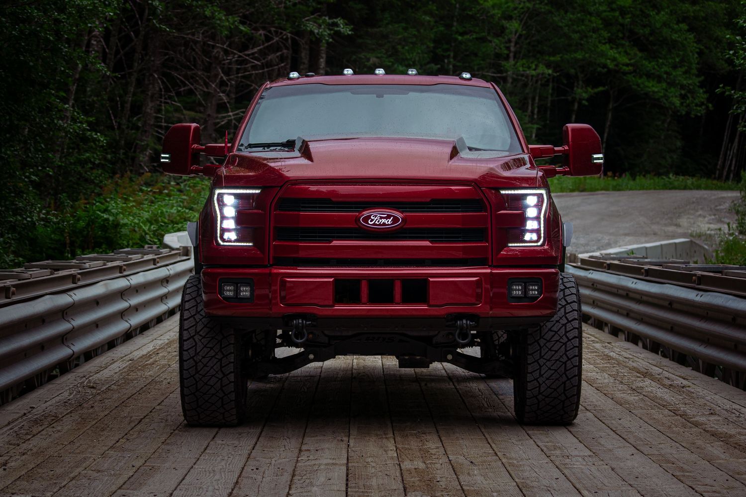 Red pickup truck crossing a wooden bridge in a wooded area.