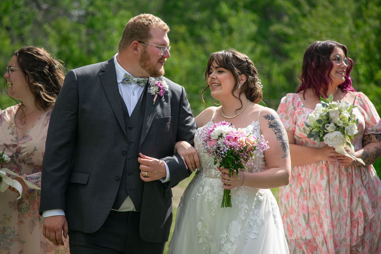 Wedding party poses outdoors with bridesmaids in pink floral dresses and white bouquets.