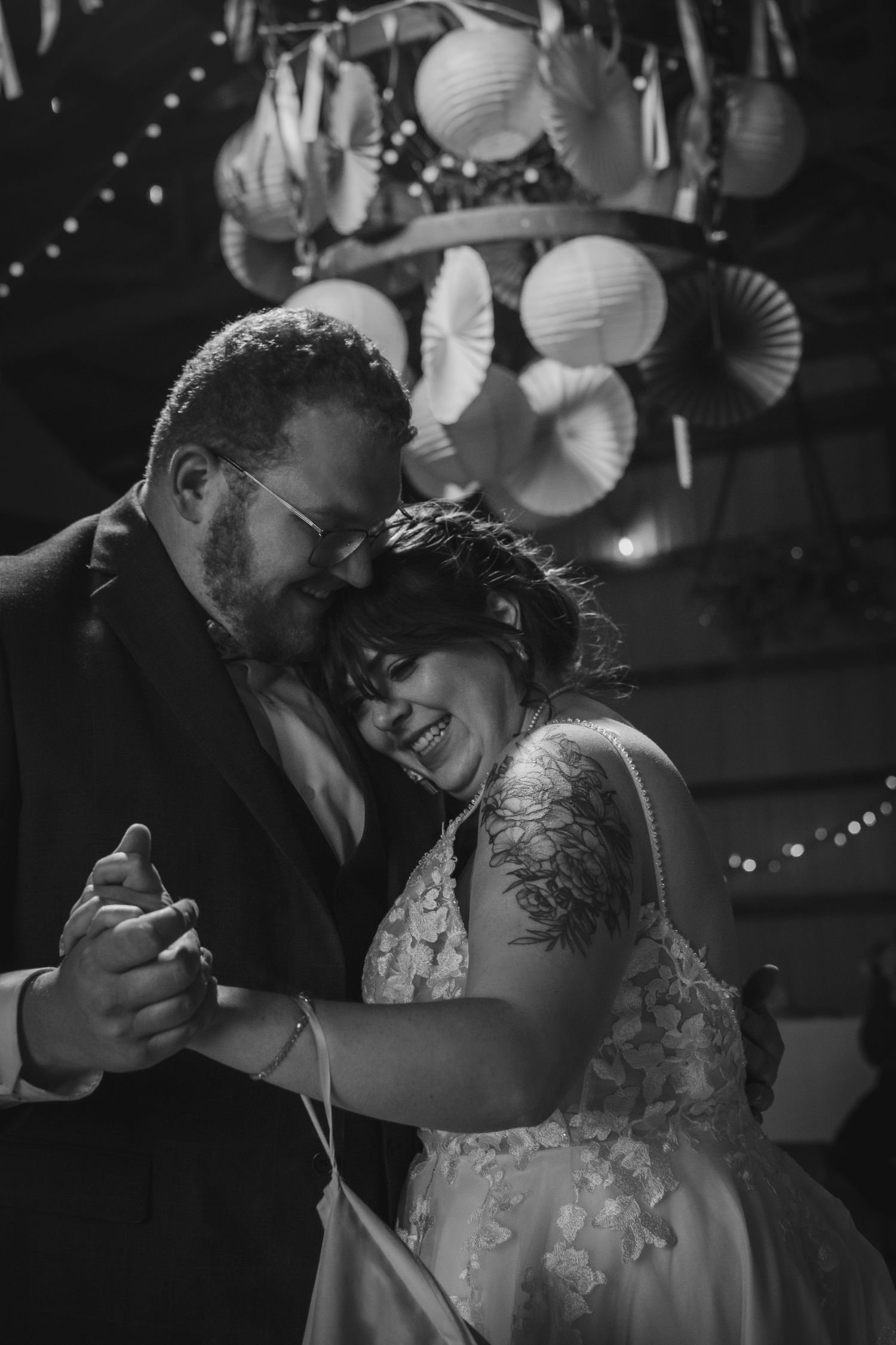 Black and white photo of newlyweds dancing intimately under paper lantern decorations.