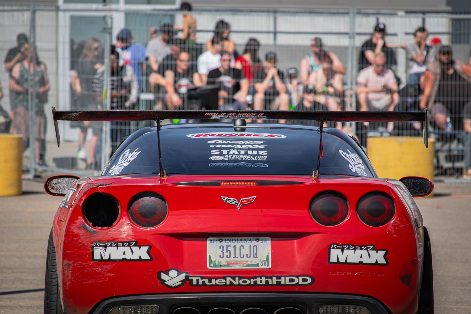 Red sports cars lined up at a racing or car show event with spectators in background.