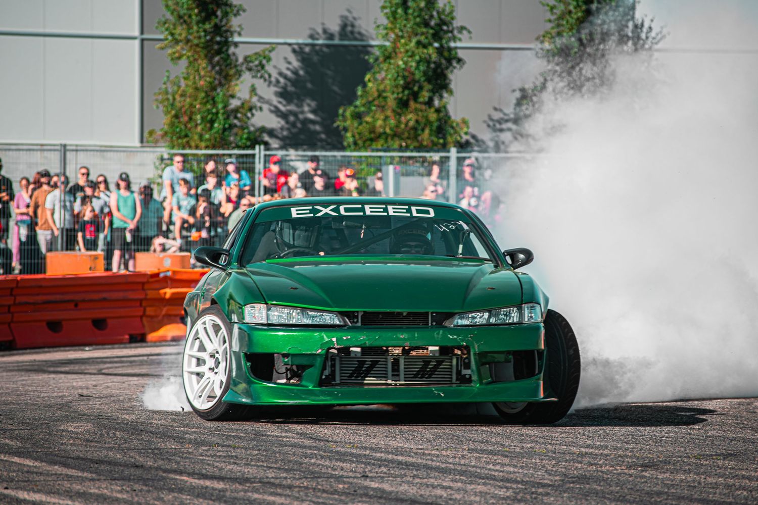 Green drift car performing a smoky burnout demonstration at a motorsport event.