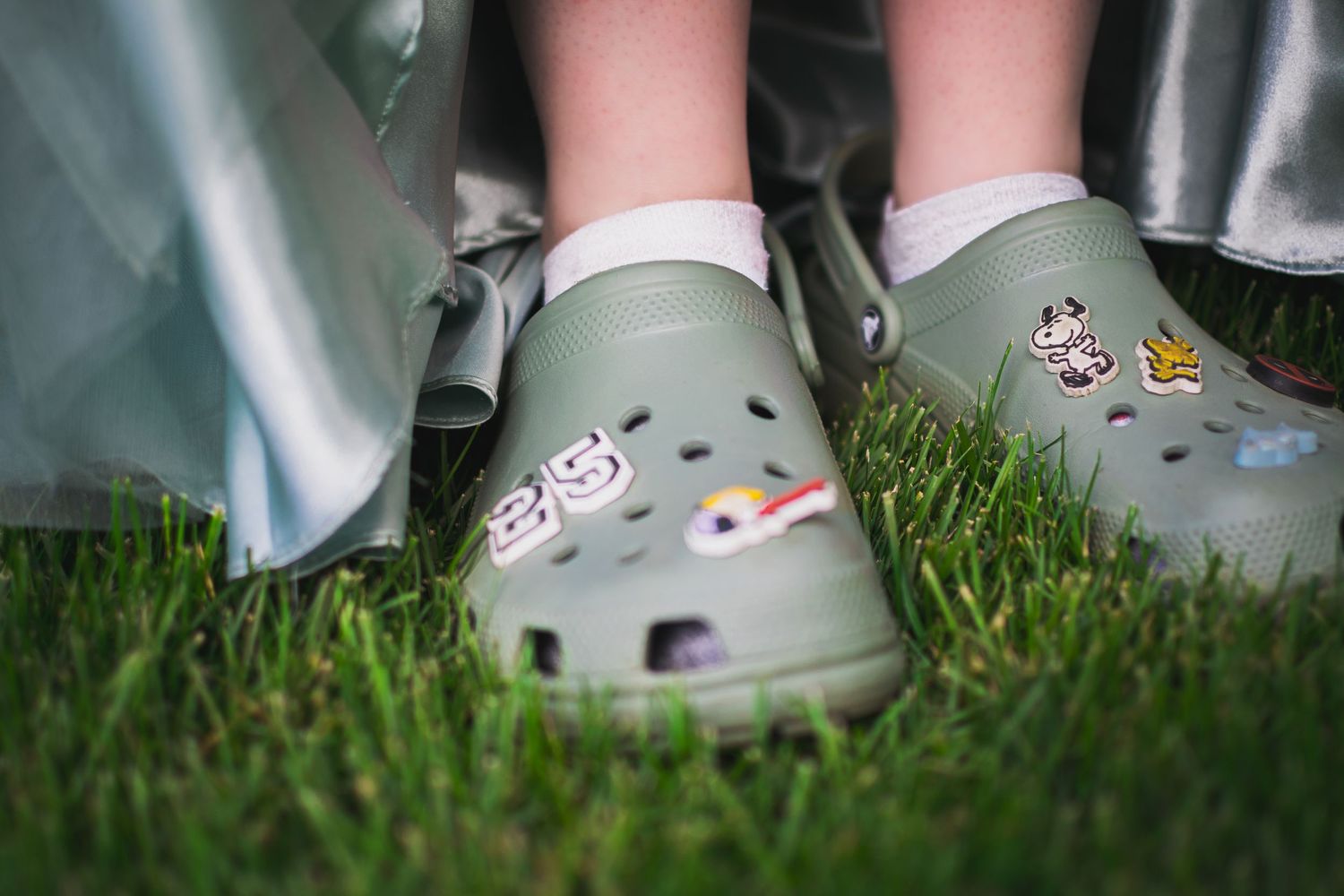 Green Crocs shoes peek out from beneath graduation regalia on grass.