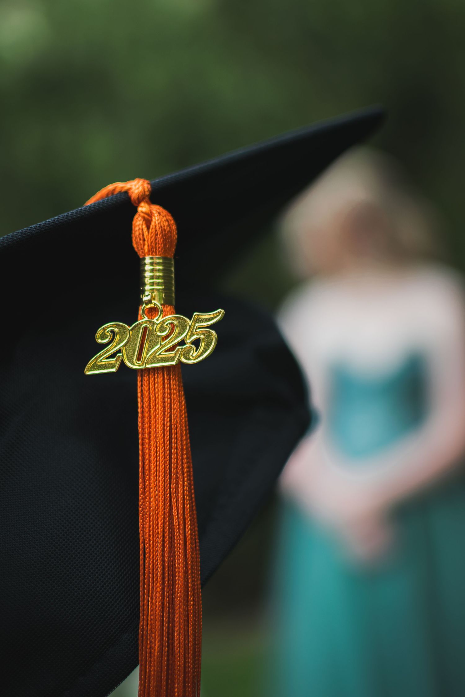 An orange graduation tassel with gold 2025 charm hangs against a black graduation cap.