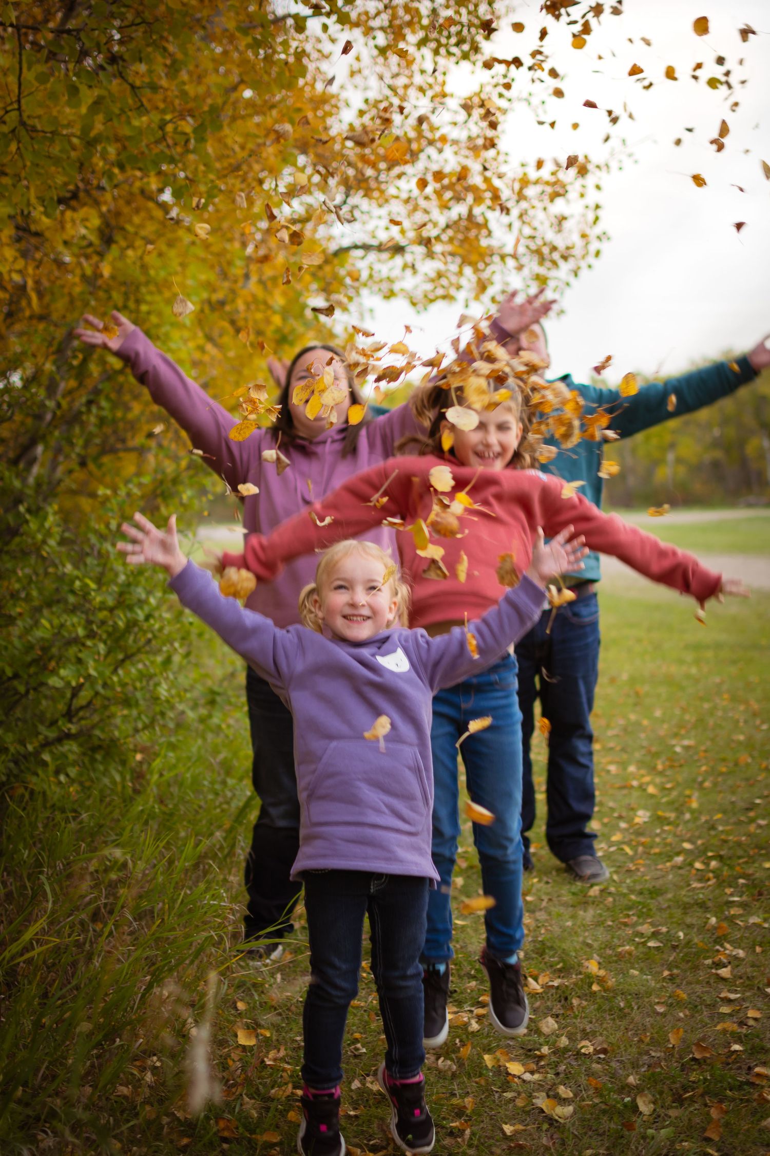 Children throw autumn leaves in the air while playing outdoors on a fall day.