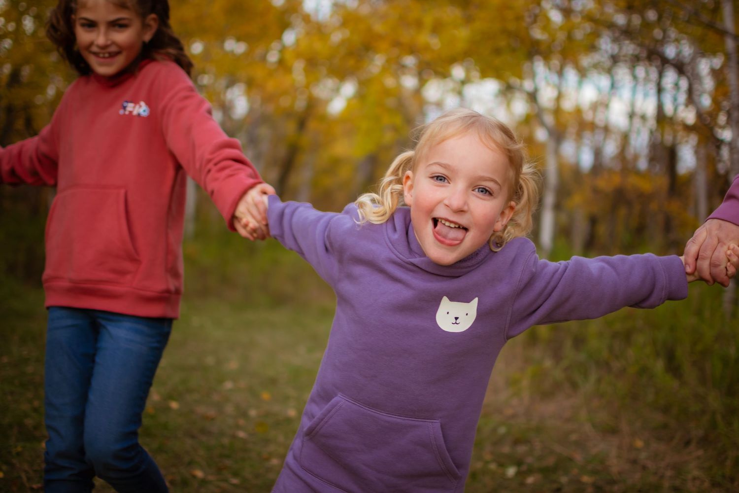Children play joyfully in fallen autumn leaves wearing colorful sweaters.