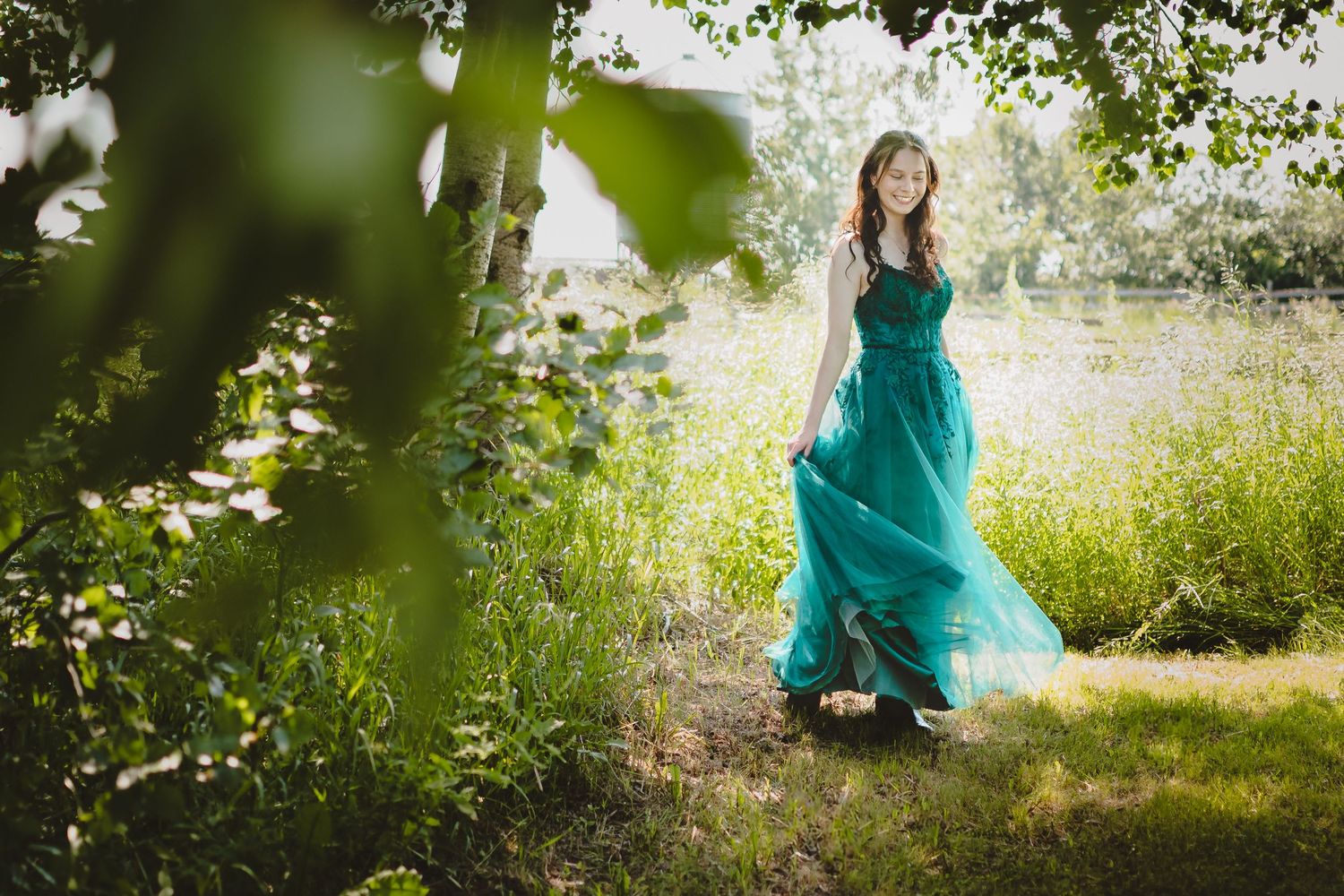 A flowing emerald green formal dress twirls gracefully in a sunlit outdoor garden setting.