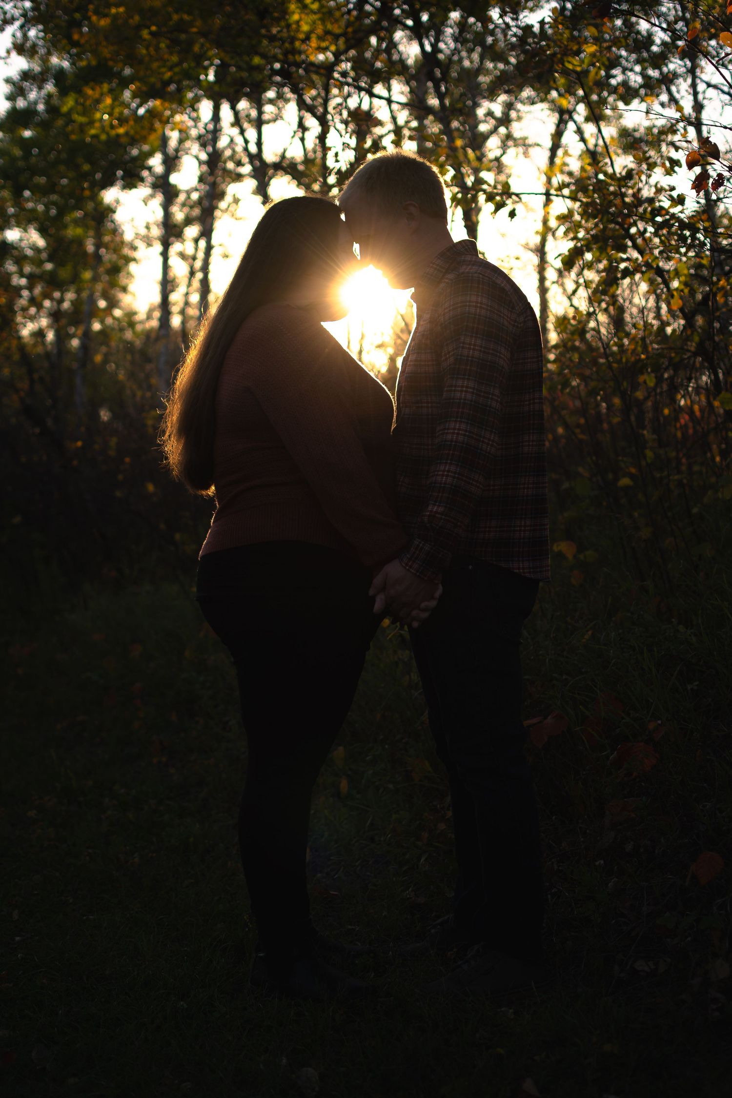 Silhouetted figures standing together against a sunset through trees.