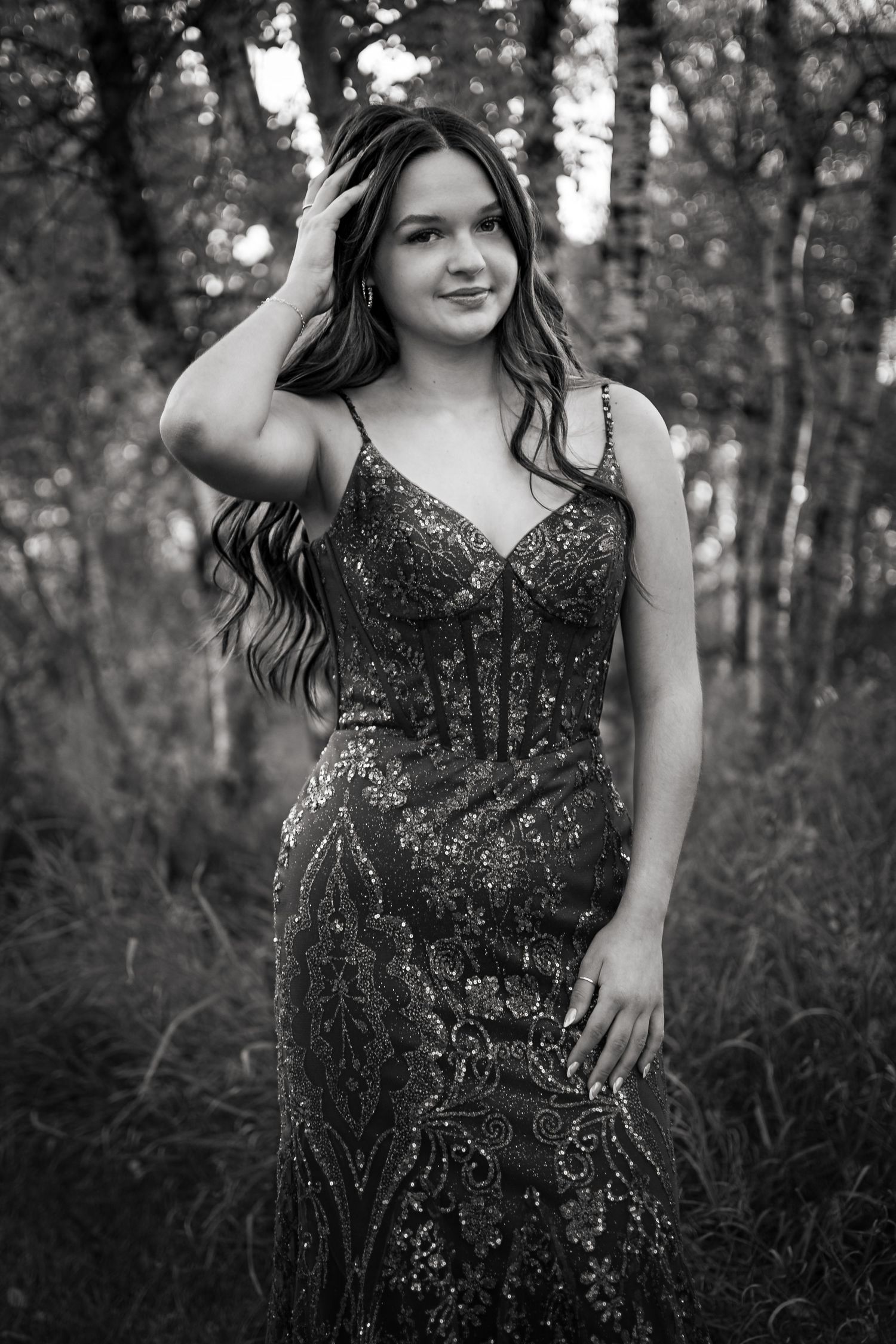 Person in a sparkly black formal dress posing in a wooded setting.