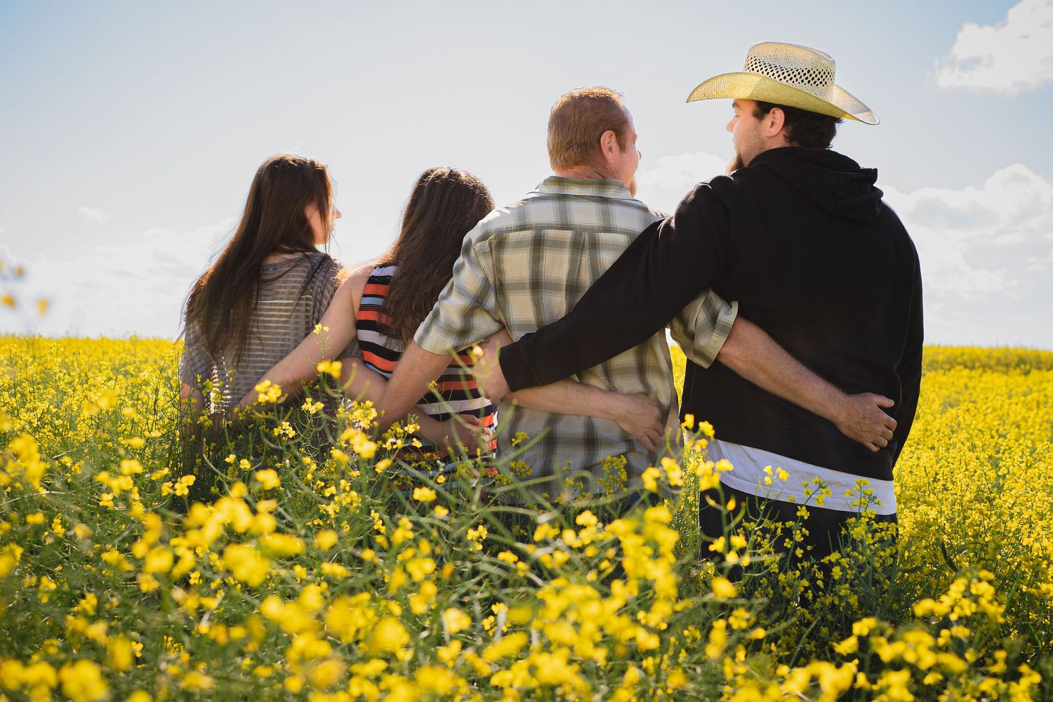 Candid family photos taken in a vibrant yellow canola flower field on a sunny day.