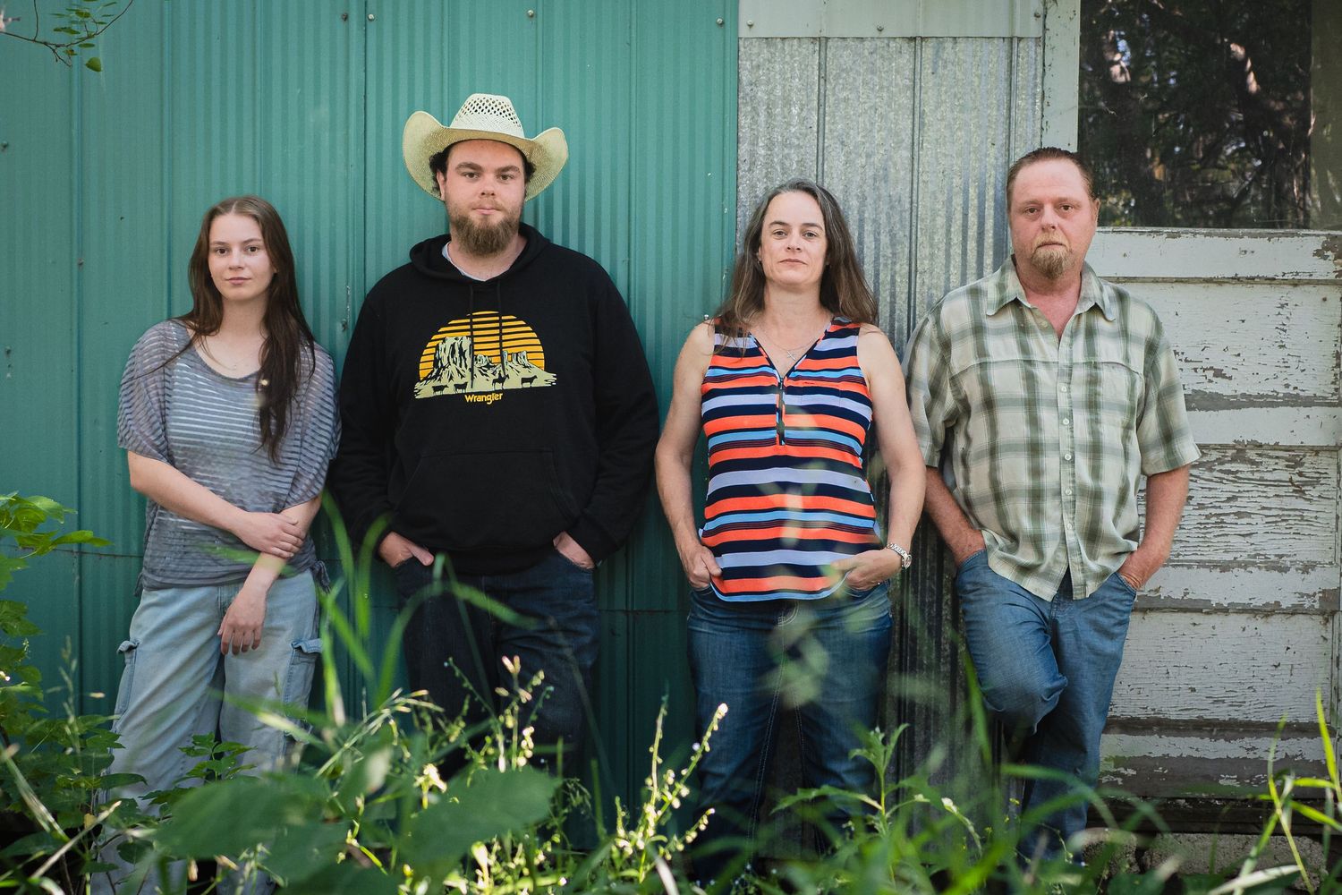 Family portrait of people posed casually against a turquoise wall outdoors.