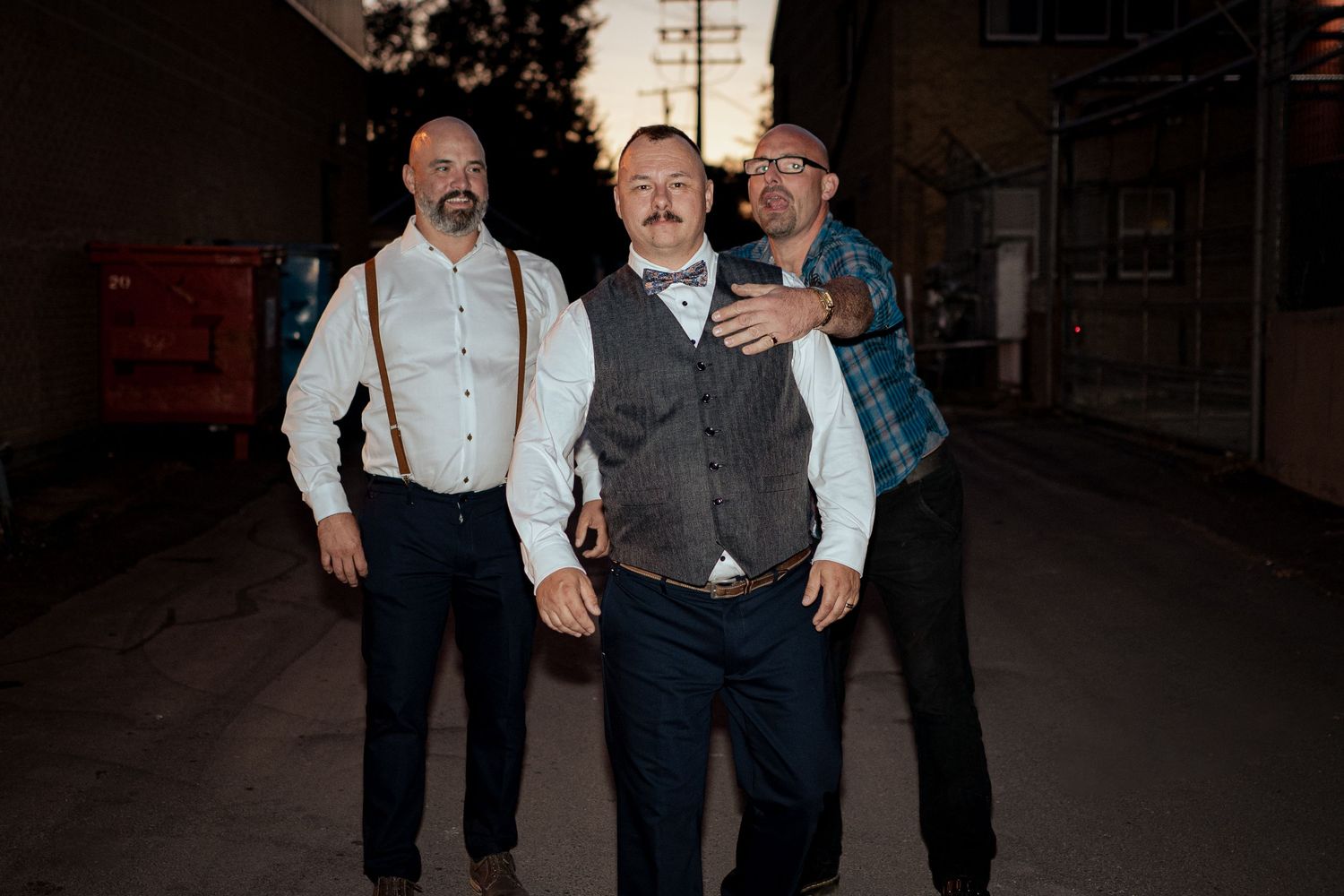 Groomsmen in formal attire share candid laughs during outdoor wedding photography session.