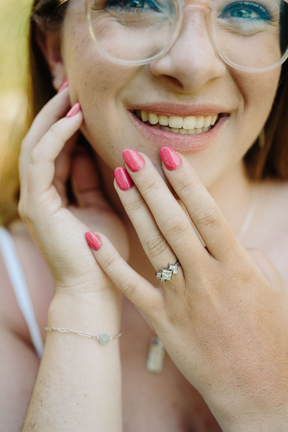Close-up photo showing hands with pink nail polish and a sparkling engagement ring.