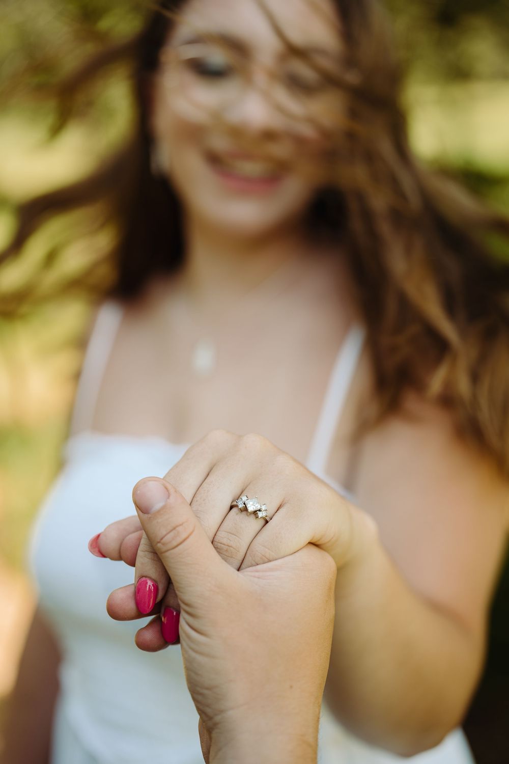 A series of hands showing off engagement rings against a soft blurred natural background.