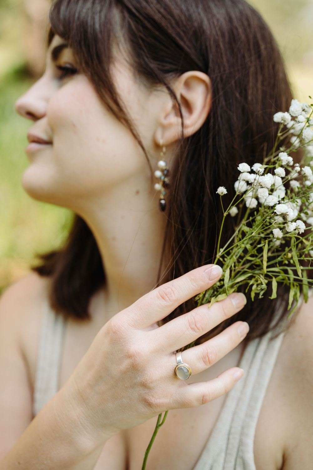 A profile view showing delicate pearl earrings and baby's breath flowers held against a natural backdrop.