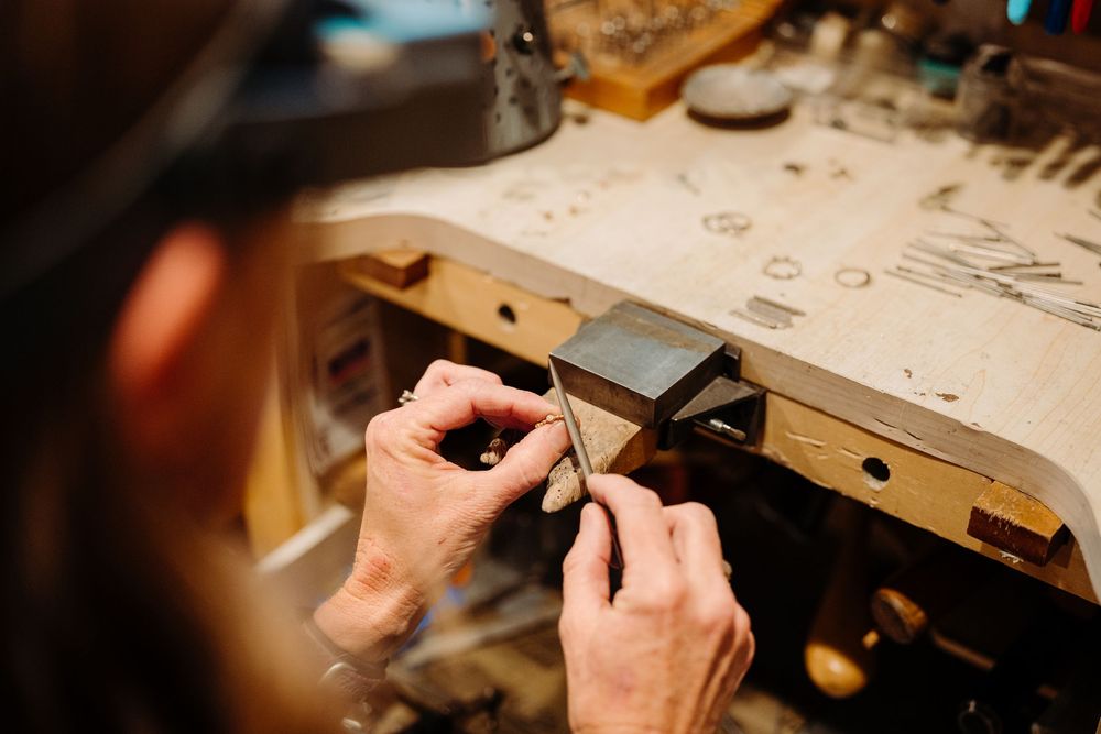Close-up of hands working with precision tools on a jewelry piece at a wooden workbench.