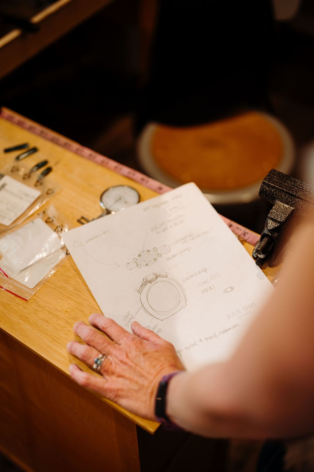Close-up view of hands sketching and drawing on white paper at a wooden desk surface.