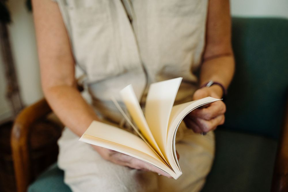A person in a white dress holds and flips through pages of a book while standing.