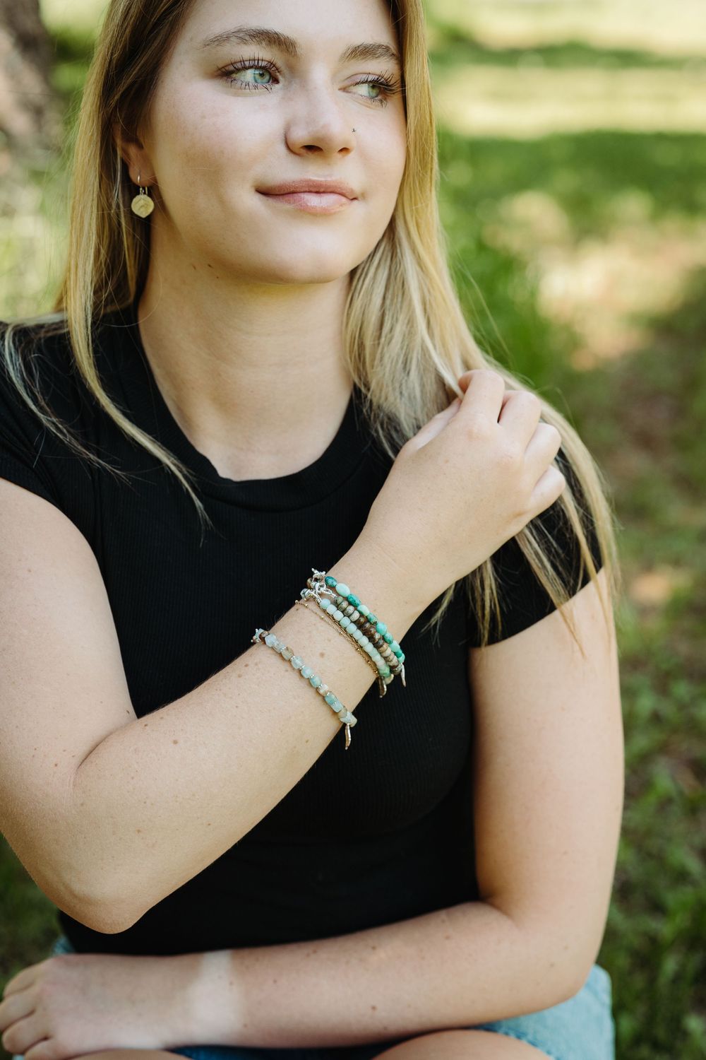 A close-up shot showing layered beaded bracelets and jewelry accessories against a natural outdoor background.