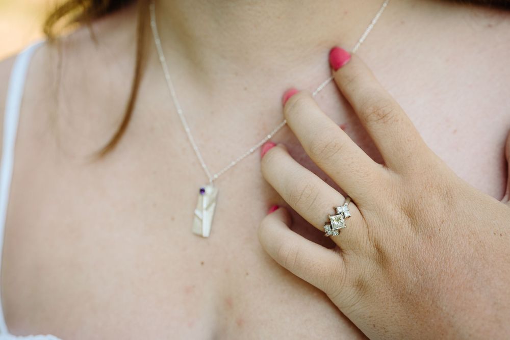 Close-up shot of hands wearing delicate silver rings with gemstones against a soft neutral background.