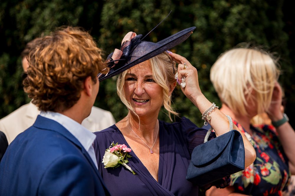 Wedding guests socialize during an outdoor reception with one wearing a navy fascinator hat.