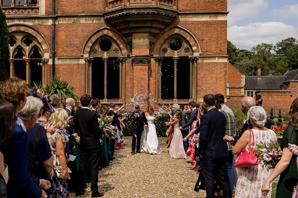 Wedding guests gather outside a historic brick building with Gothic arches during the ceremony.