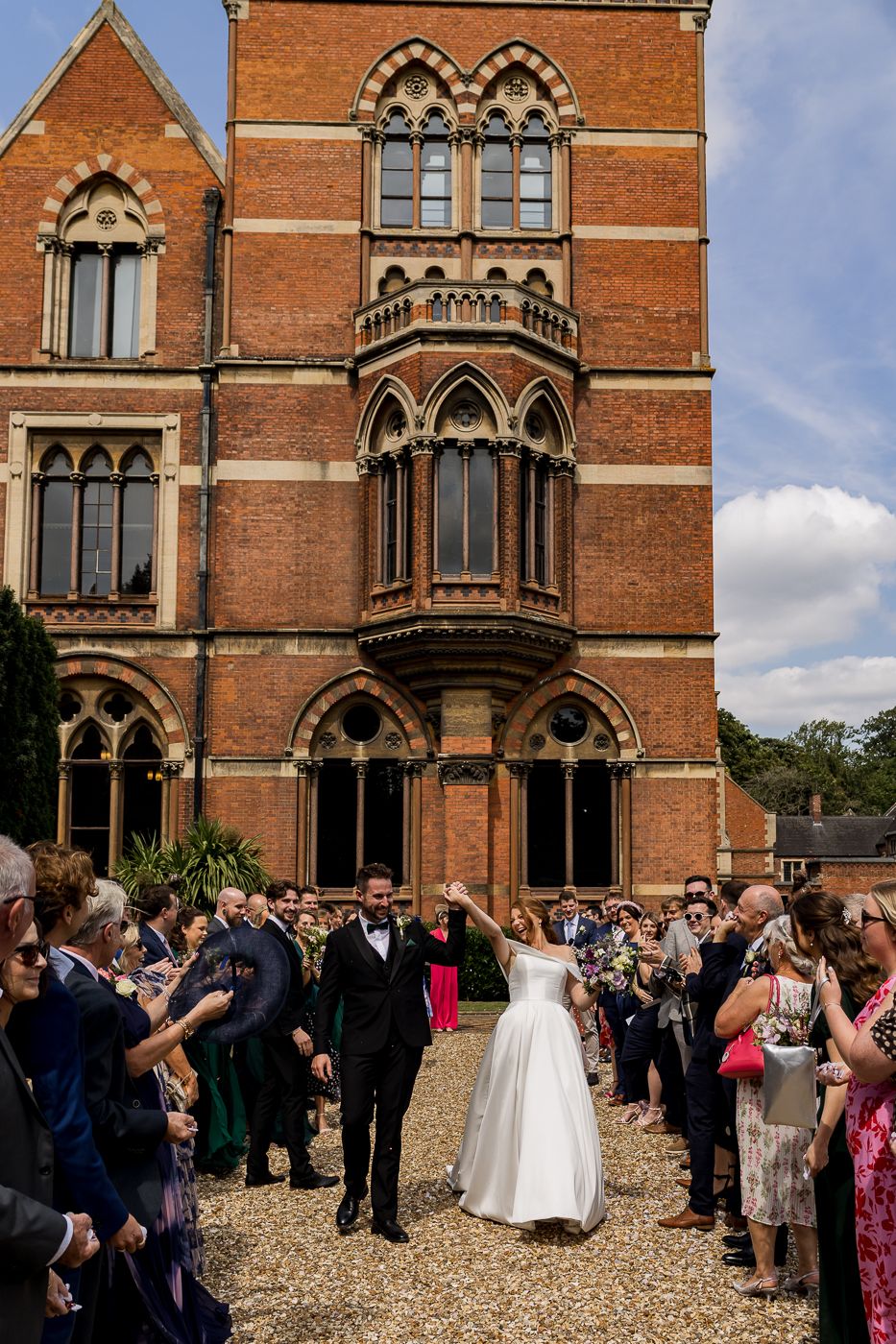 Wedding celebration with guests lined up along path at Victorian Gothic building entrance.
