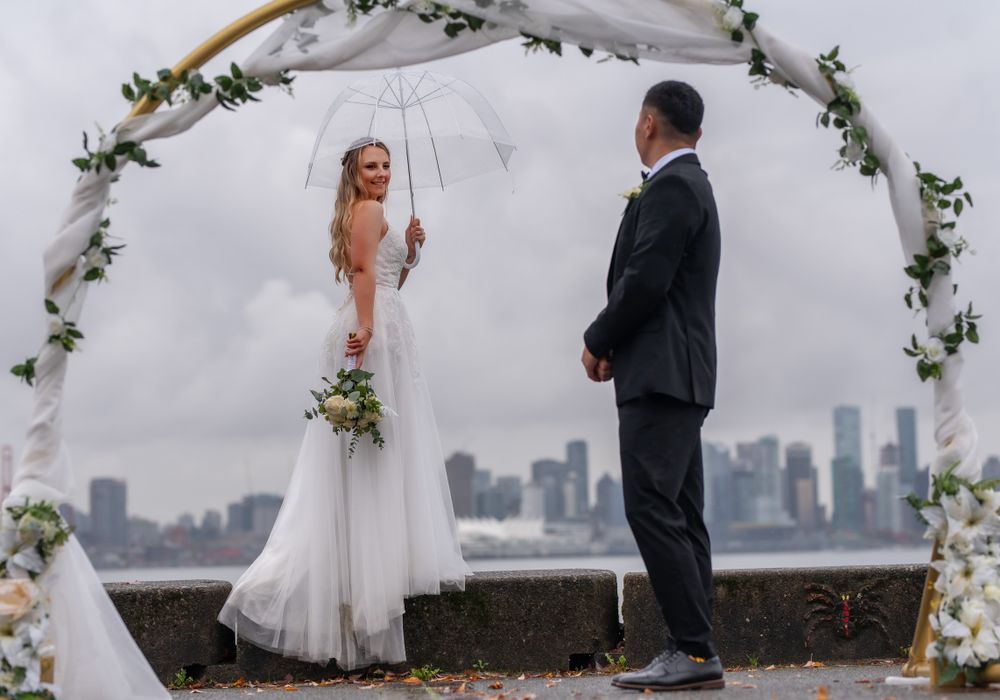 Wedding ceremony under a floral arch with city skyline backdrop.