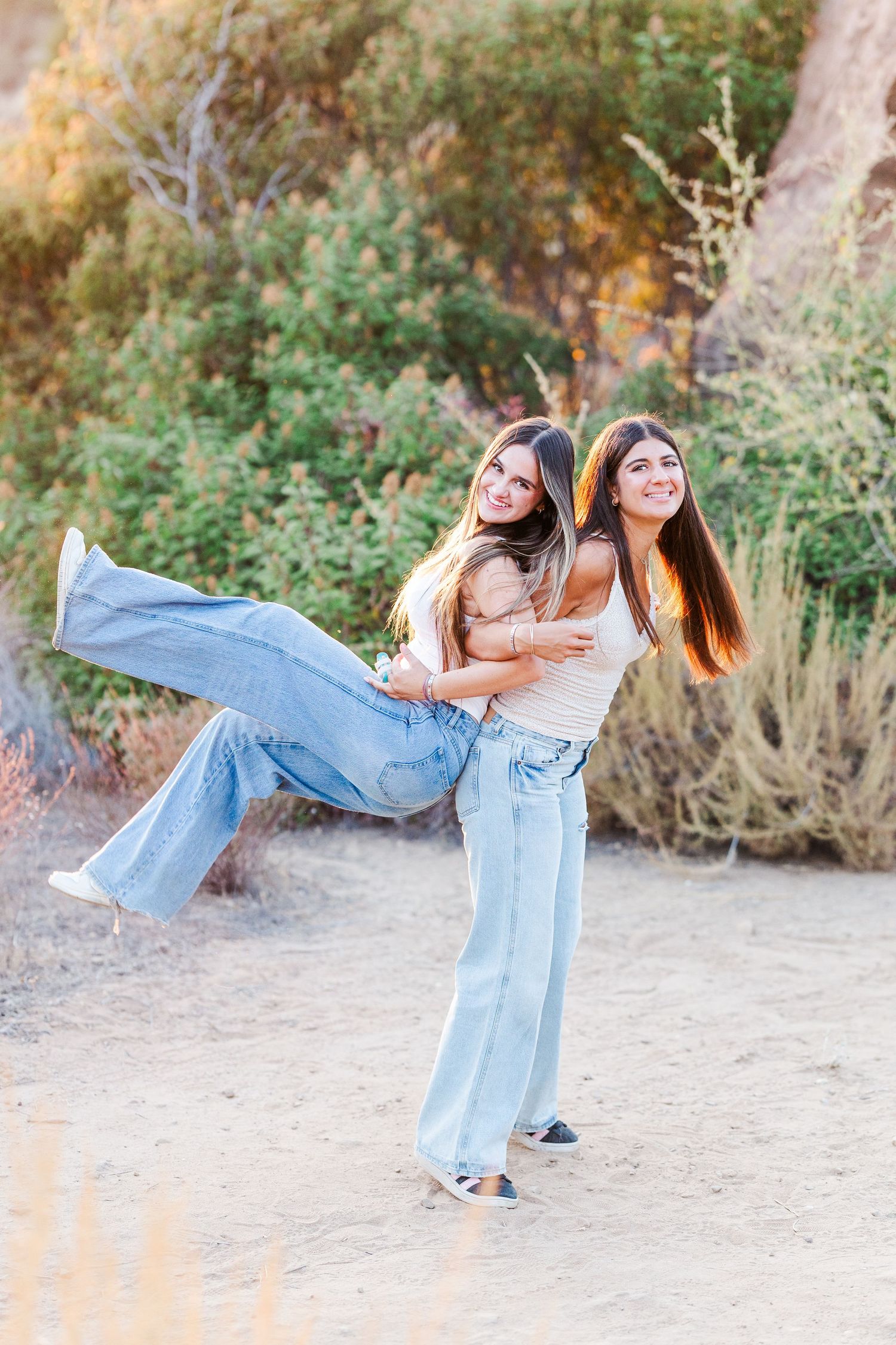 Two dancers perform a synchronized back-bending dance move outdoors against a natural backdrop.