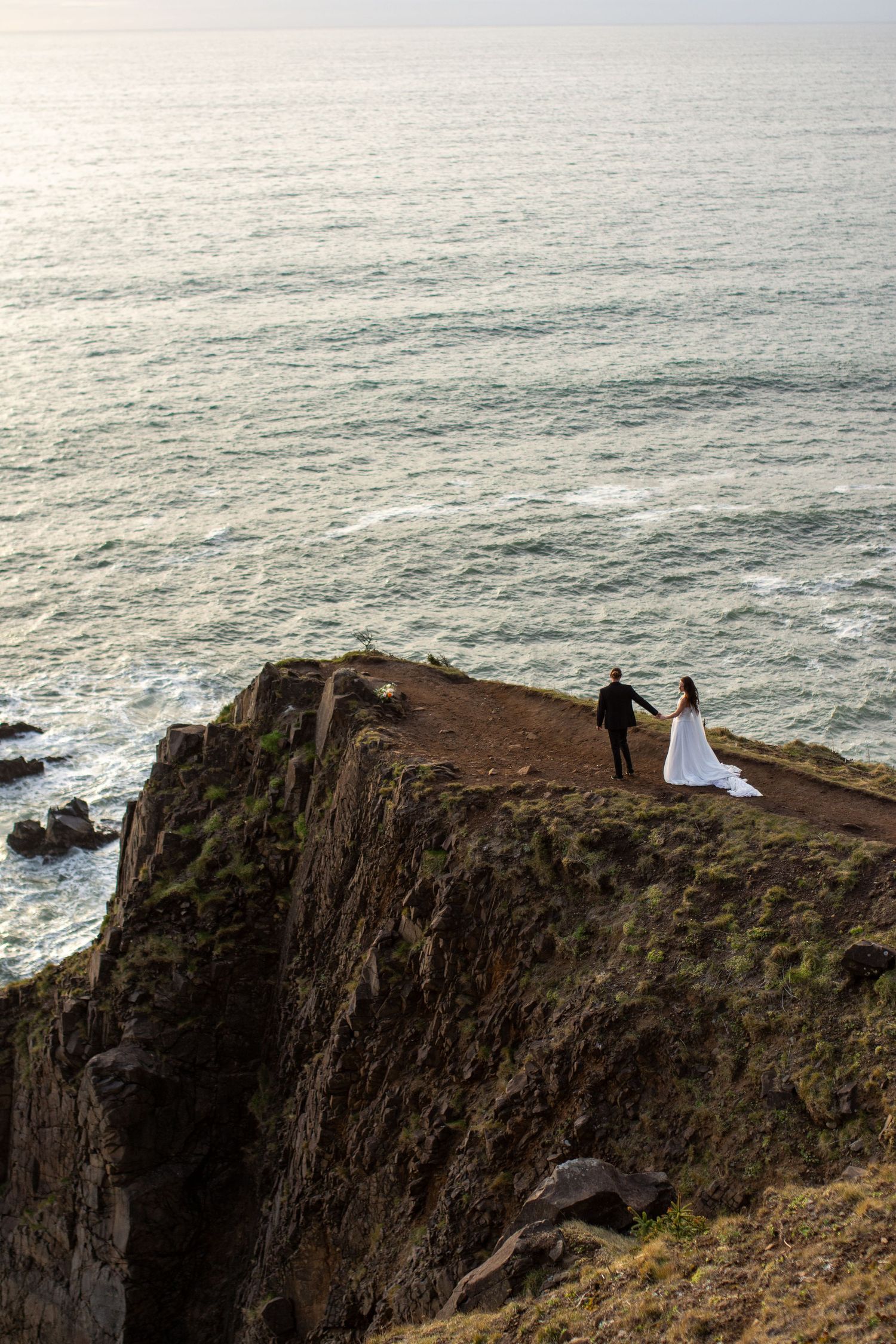 Dramatic coastal cliff wedding photos with ocean waves crashing below.