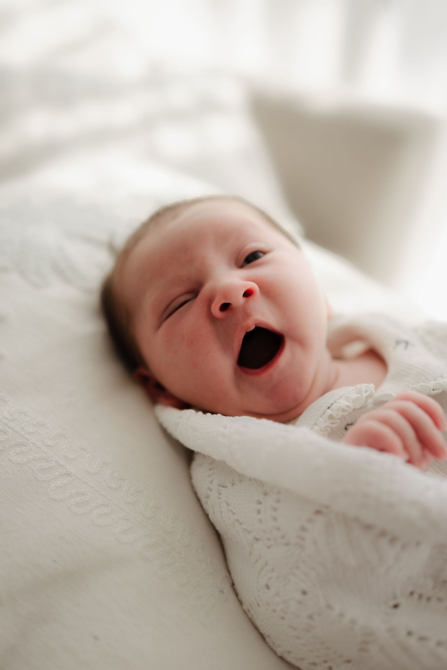 A newborn baby wrapped in white lace blanket shows different expressions from sleeping to yawning.