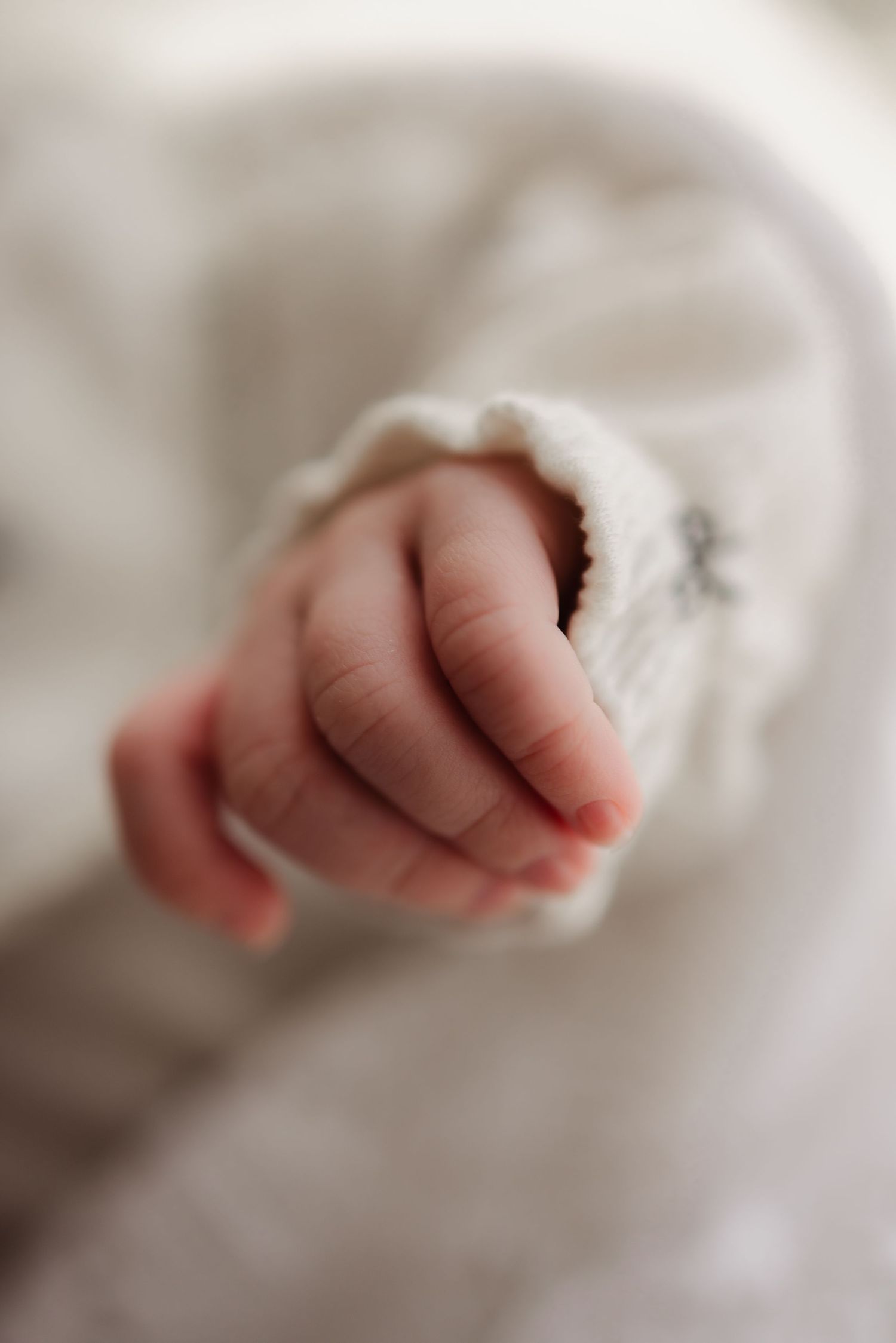 Close-up of tiny newborn baby hands grasping white fabric.