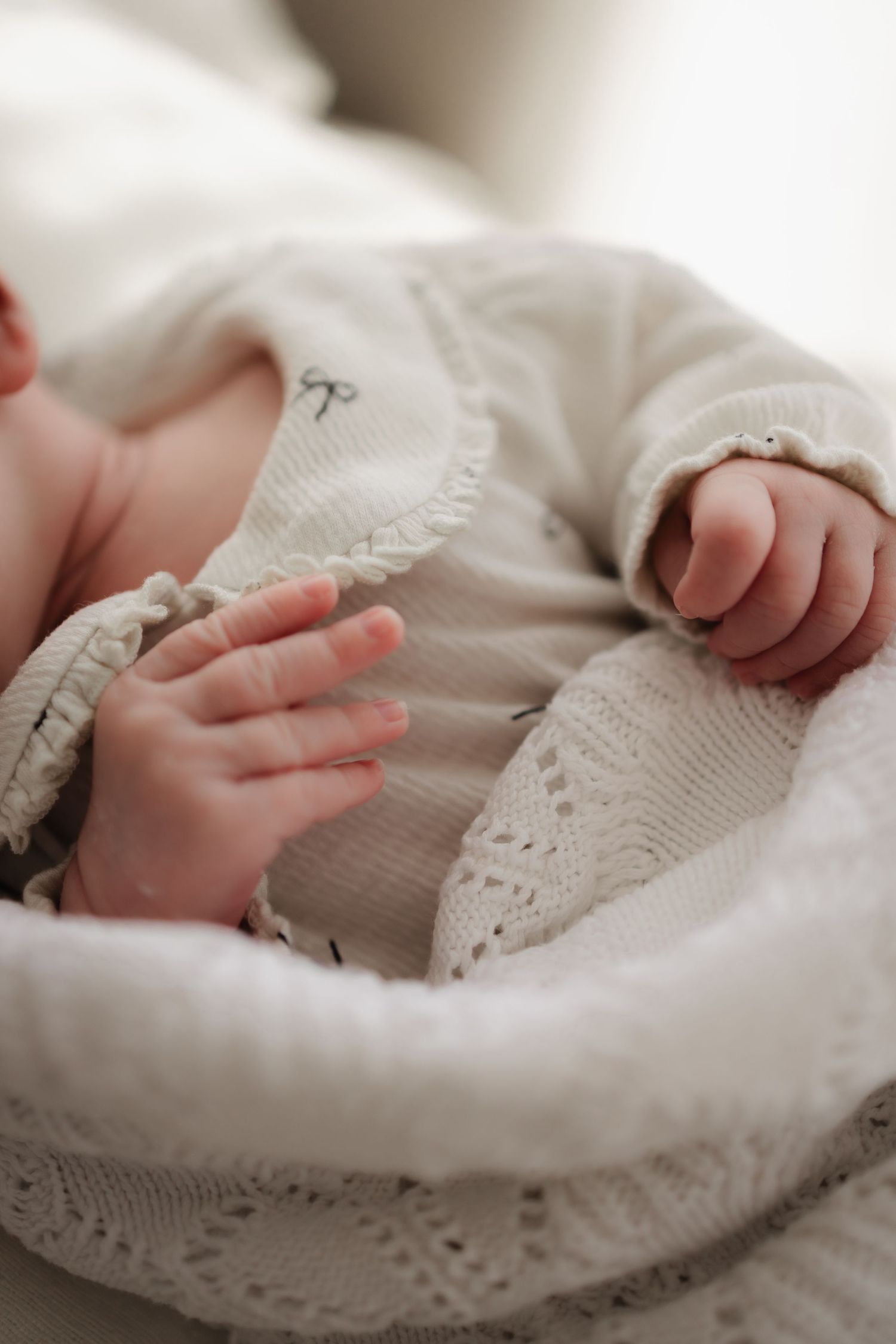 Tiny baby hands and fingers peek out from delicate white lace swaddle blanket.