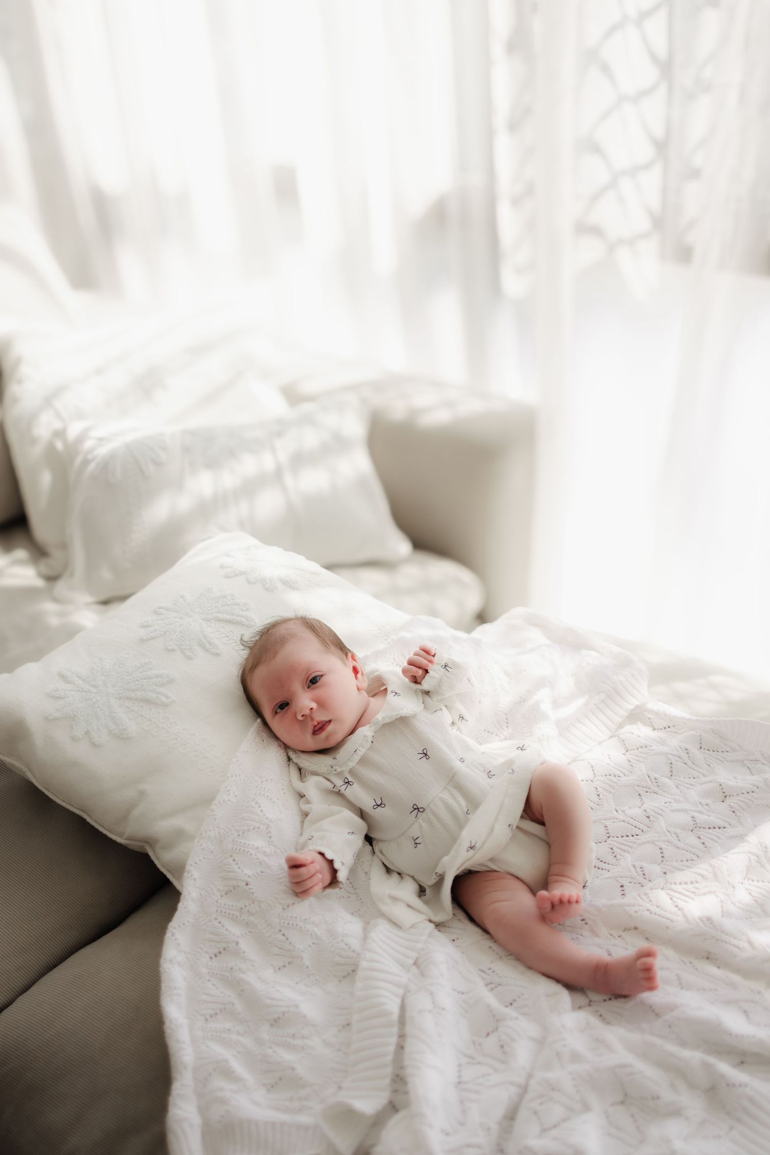 A baby in white clothing rests peacefully on soft white bedding in a series of gentle poses.