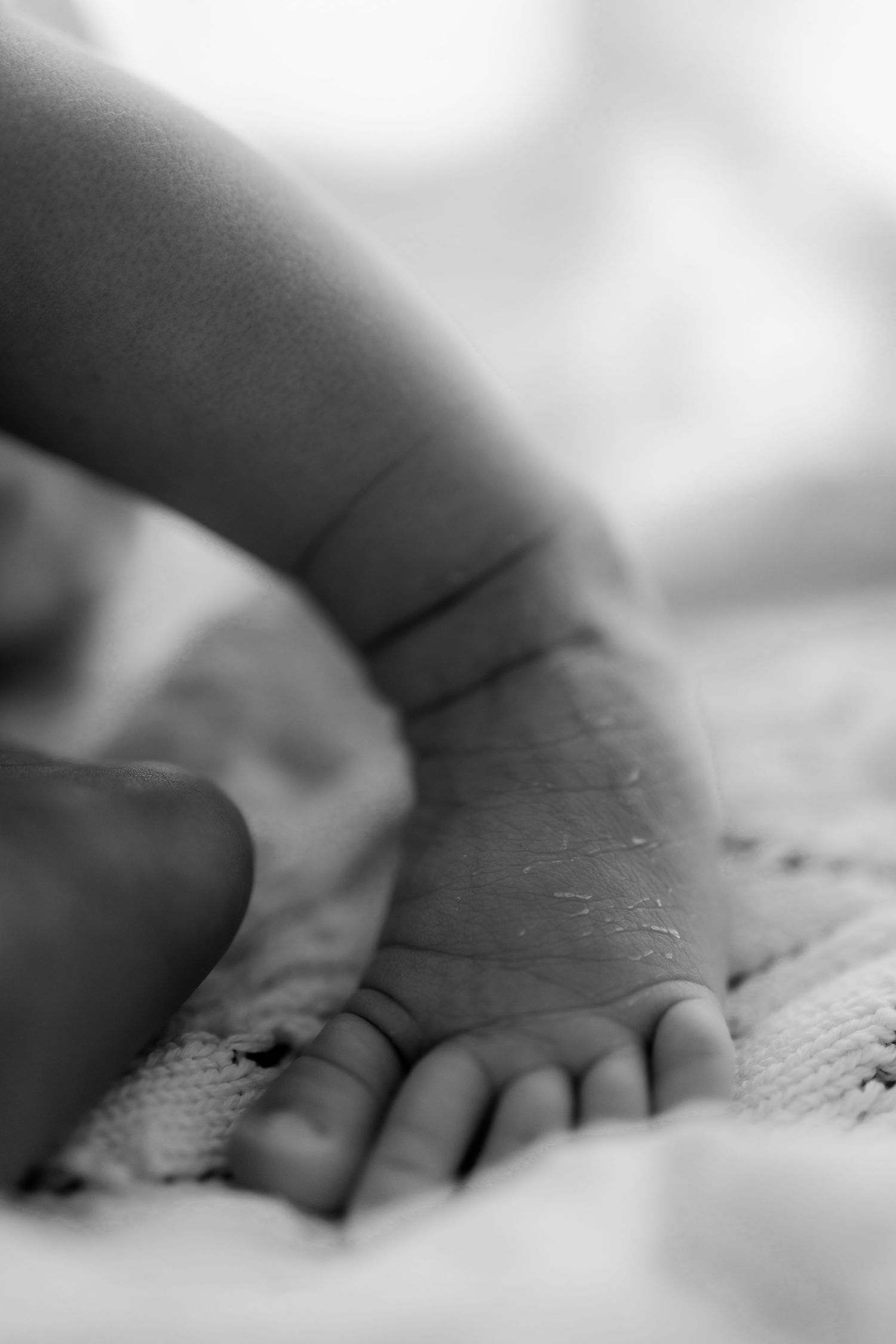 Close-up black and white photograph of a tiny newborn baby hand resting on textured fabric.